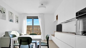 Una cocina moderna con comedor, muebles blancos y un amplio ventanal con cortinas.