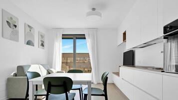Una cucina moderna con zona pranzo, mobili bianchi e un'ampia finestra con tende.