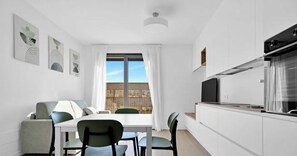 A modern kitchen with a dining area, white cabinetry, and a large window with curtains. - [COM44] Historic Milan: Bright Apartment (Milano)