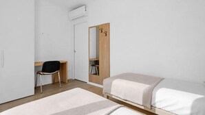 Una habitación minimalista con escritorio, silla, dos camas, armario y espejo.