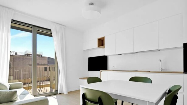 Un apartamento moderno con zona de comedor, cocina con armarios blancos y un amplio ventanal corredera a un balcón.