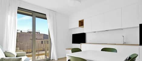 A modern apartment with a dining area, a kitchen with white cabinets, and a large sliding glass door to a balcony.