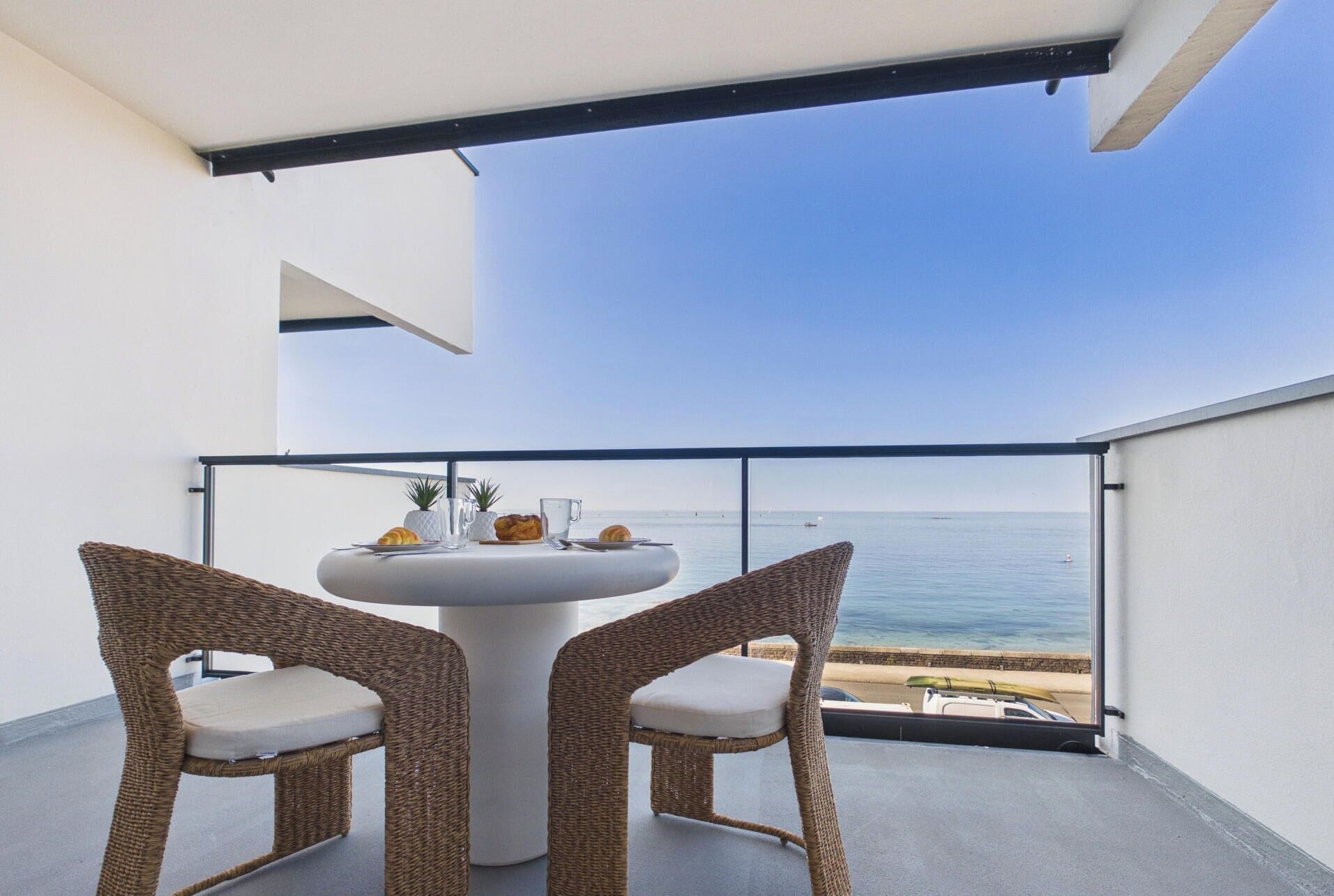 Ein Balkon mit zwei Korbstühlen, einem runden Tisch und Blick aufs Meer.