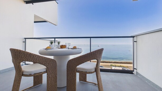 A balcony with two wicker chairs, a round table, and a view of the sea. - -OPALE- Studio with ocean view, balcony, and parking (Concarneau)