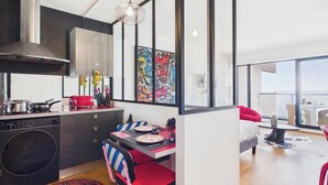 A modern kitchen with a built-in oven, a dining area with a table and chairs, and a large window offering a view of the city. - -OPALE- Studio with ocean view, balcony, and parking (Concarneau)