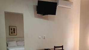 A hotel room with a bed, a desk, a chair, a TV mounted on the wall, and an air conditioning unit. - Oro Boutique Guesthouse  (Matola)