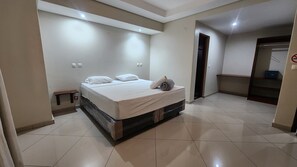 Una habitación de hotel con una cama, una mesita de noche, una puerta e interruptor de luz en la pared.