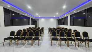 Un salón de conferencias con hileras de sillas, ventanas amplias e iluminaci ón del techo en azul.