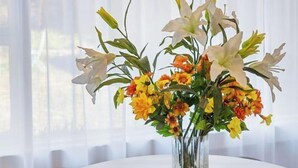 Ein runder Esstisch mit einer Blumenvase in der Mitte, umgeben von Korbstühlen.