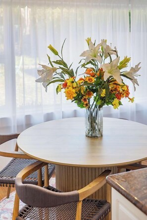 A round dining table with a vase of flowers in the center, surrounded by wicker chairs. - Charming Garden Retreat: Peaceful Oasis with Vintage Character (Dalkeith)