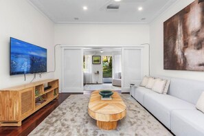 A modern living room with a large flat-screen TV, a wooden coffee table, a white sofa, and a large abstract painting on the wall.