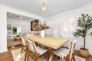 A dining area with a wooden table, six chairs, a vase with flowers, and a potted plant.