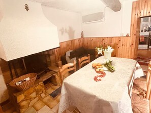 Ein rustikaler Essbereich mit Kamin aus Stein, Holzwänden und einem Tisch, der mit Früchten und Blumen gedeckt ist.