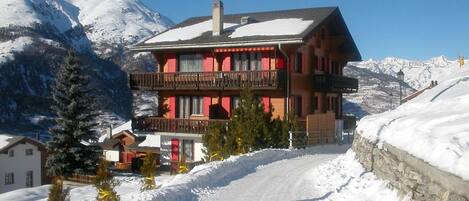 Eine zweistöckige Chalet mit Balkon, umgeben von schneebedeckten Bergen.