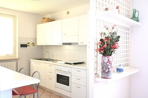 Une cuisine avec des meubles blancs, une cuisinière et un évier. Un vase rempli de fleurs est posé sur le comptoir.