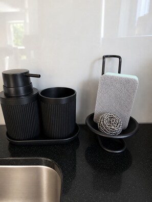 A kitchen area with a stainless steel sink, black kitchen accessories, and a towel holder with a towel.
