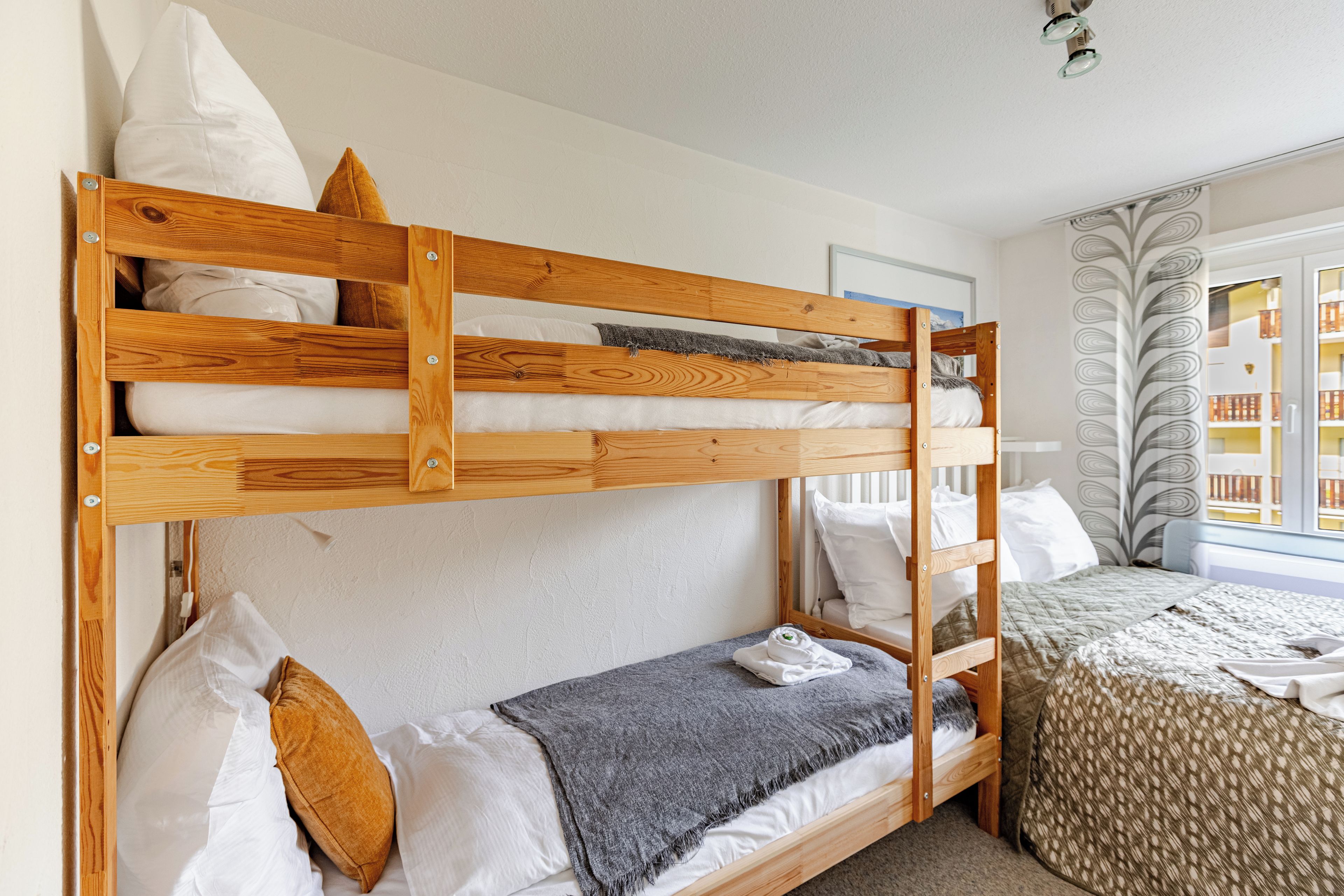 Ein Etagenbett mit Holzrahmen, weißer Bettwäsche und einer grauen Decke.