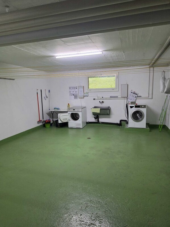 A laundry room with two washing machines, a window, and a green floor.