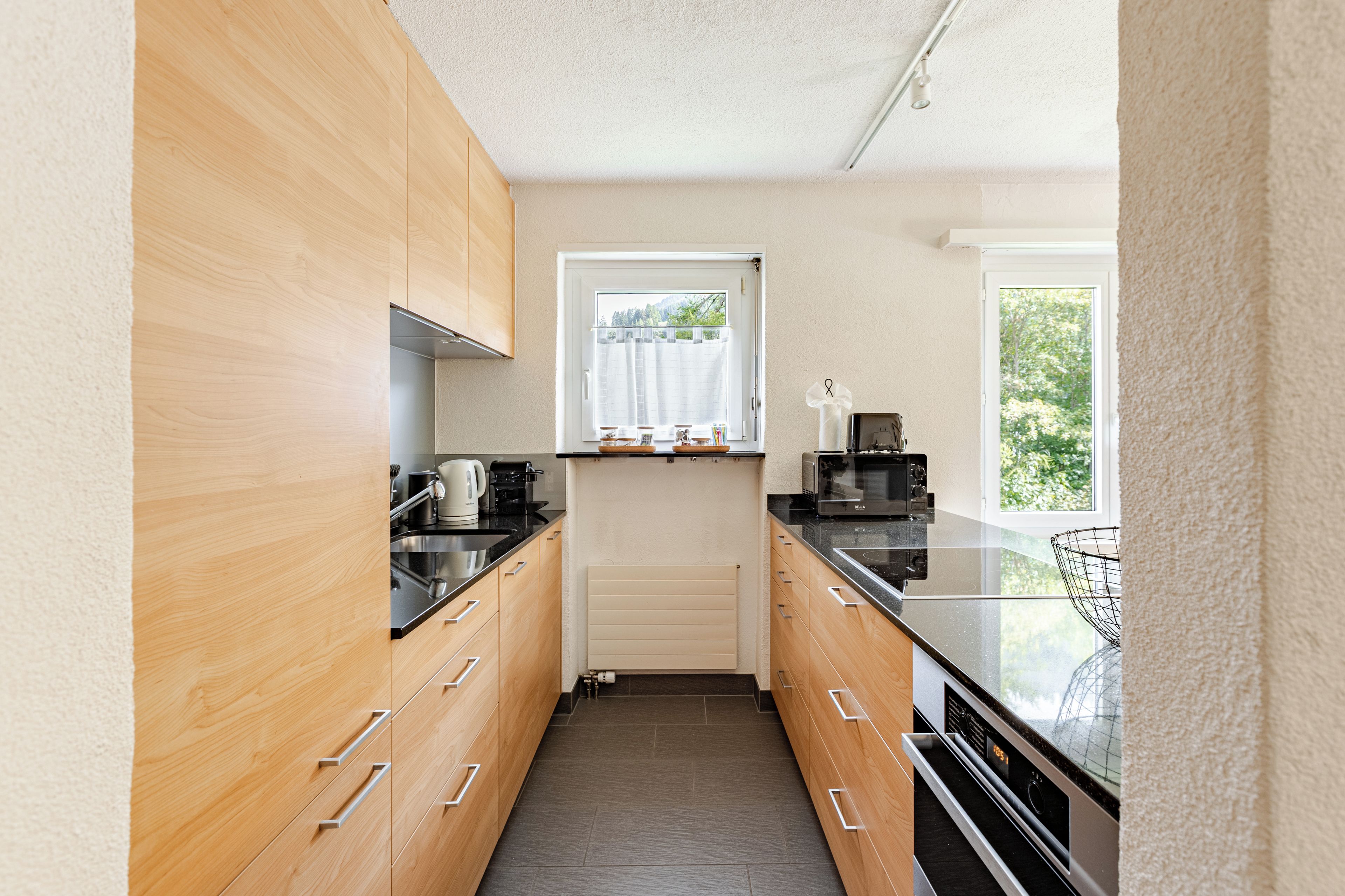Une cuisine moderne avec des meubles en bois, un plan de travail noir et une fenêtre donnant sur un paysage verdoyant.