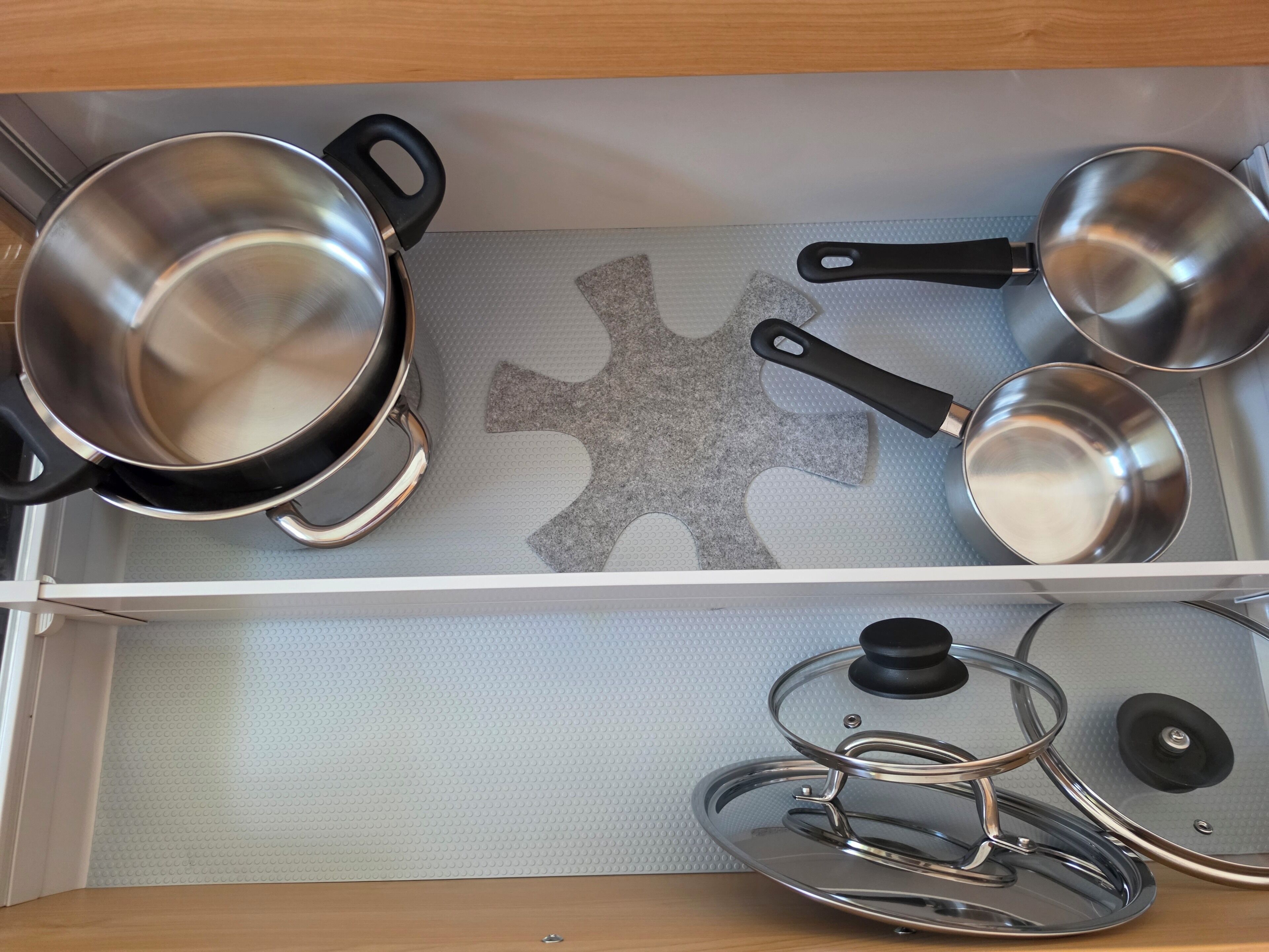 Eine Küchenschublade mit Edelstahl-Töpfen, -Pfannen, einem Wasserkocher und einem Sieb.