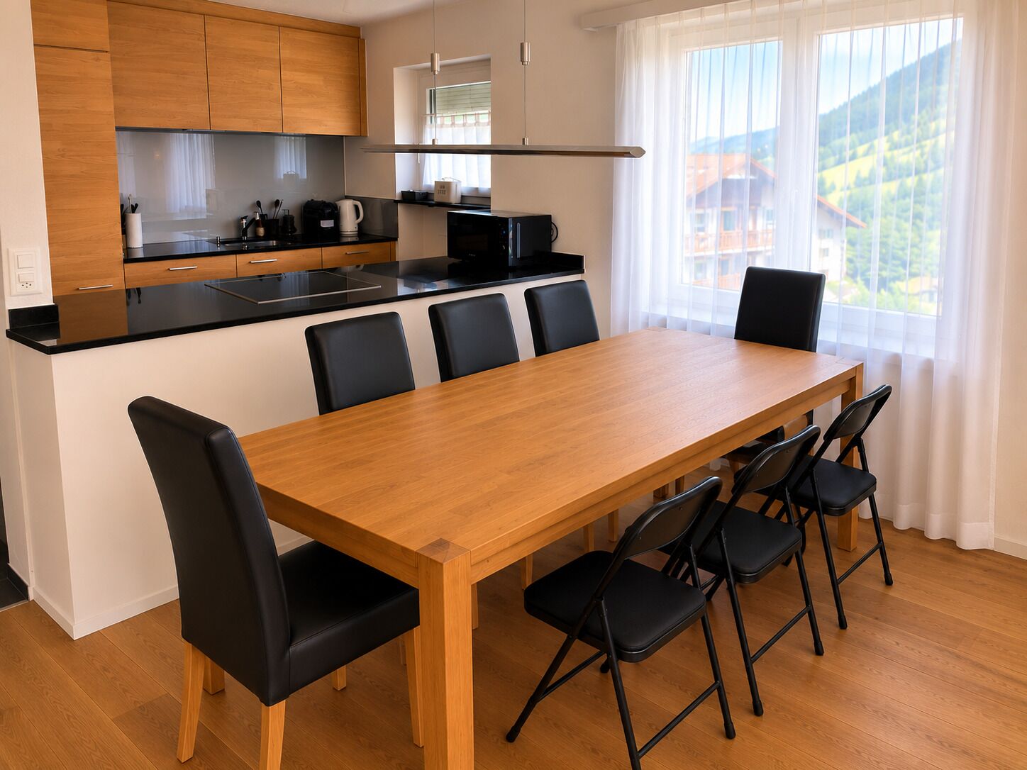 A modern kitchen with wooden cabinets, a black countertop, and a dining area with a wooden table and black chairs.