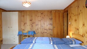 Una habitación con paneles de madera, dos camas, una mesa con mantel a cuadros y una silla.