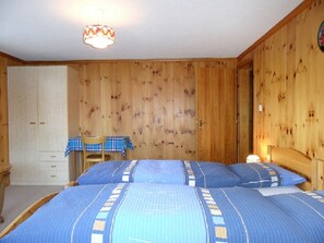 Ein Zimmer mit Holzwänden, zwei Betten, einem Tisch mit kariertem Tuch und einem Sessel.