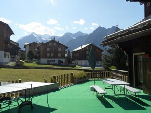 A courtyard with tables and benches, surrounded by buildings and mountains in the background. - Ferienwohnungen Chalet Matten, (Grächen), by Interhome (Grächen)