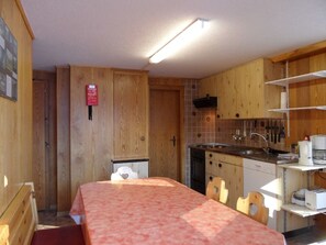 Eine kleine Küche mit Holzschränken, einem Spülbecken und einem Essbereich mit Tisch und Stühlen.