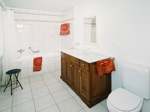 Ein Badezimmer mit weißem Waschbecken, Holzschrank, Toilette und Duschbereich.