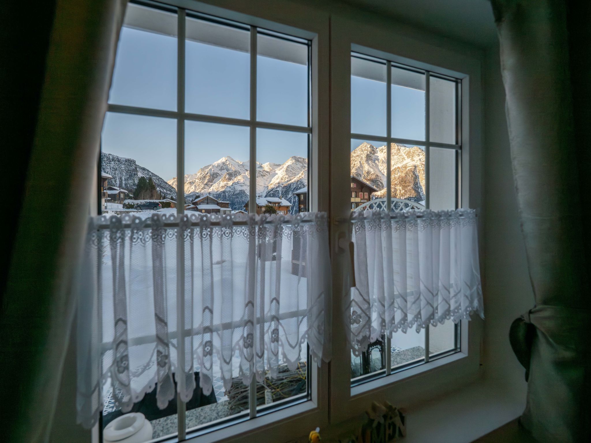 A window with a view of snow-covered mountains and a wooden building.