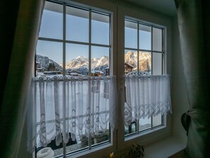 Ein Fenster mit Blick auf verschneite Berge und ein Holzbäude.