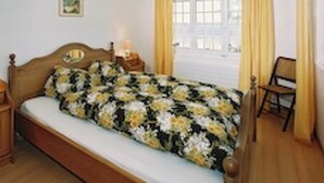 A bedroom with a bed, a nightstand, a chair, a window with curtains, and a picture on the wall. - Edelweiss, (Grächen), 5051 by Interhome (Grächen)
