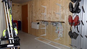A room with wooden walls, a door, and various items including skis, a snowboard, and a pair of red boots. - Chalet Matten, (Grächen), by Interhome (Grächen)