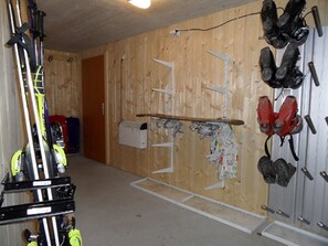 Ein Zimmer mit Holzwänden, einer Tür sowie verschiedenen Gegenständen, darunter Ski, ein Snowboard und ein Paar rote Stiefel.