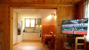 A cozy wooden interior with a dining area, kitchen, and a television displaying a sports event. - Chalet Matten, (Grächen), by Interhome (Grächen)