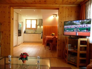 Ein gemütliches Holzambiente mit Essbereich, Küche und Fernseher, der ein Sportevent zeigt.