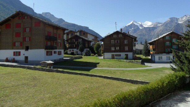 A residential area with multi-story buildings, a grassy courtyard, and a mountain backdrop. - Chalet Matten, (Grächen), by Interhome (Grächen)