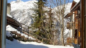 A snowy mountain landscape with a wooden building featuring balconies. - Alicia, (Grächen), 1901 by Interhome (Grächen)
