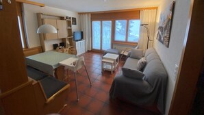 A compact living space with a bed, a sofa, a small table, a TV, and a window. - Alicia, (Grächen), 1901 by Interhome (Grächen)