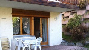 A patio with a table and chairs, a sliding glass door, and a brick pathway. - Alicia, (Grächen), 1901 by Interhome (Grächen)