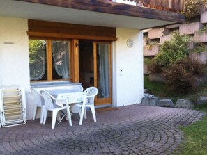 A patio with a table and chairs, a sliding glass door, and a brick pathway. - Alicia, (Grächen), 1901 by Interhome (Grächen)