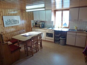 A compact kitchen with wooden walls, a dining table with chairs, a sink, and a stove. - Sunnuschy, (Grächen), 1056 by Interhome (Grächen)