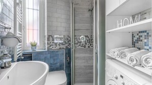 Ett modernt badrum med ett fristående badkar, en toalett, en dusch med ingång från sidan och en inbyggd tvättmaskin.