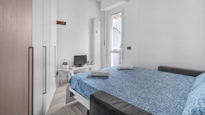 Ett sovrum med en säng, ett skrivbord, en stol, en tv och ett fönster.