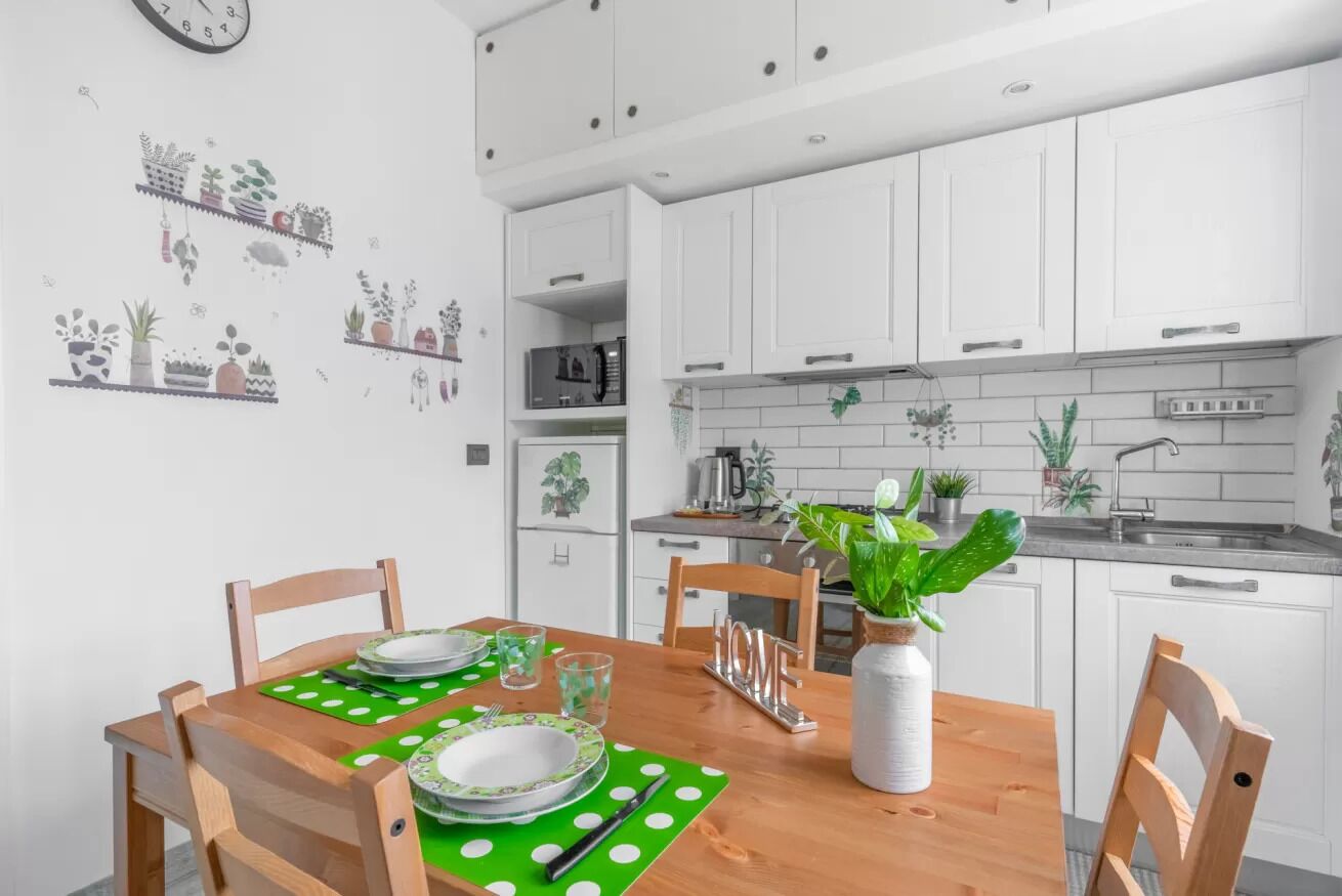 Una cucina moderna con mobili bianchi, un tavolo da pranzo in legno con sottopiatti verdi e diversi elettrodomestici.