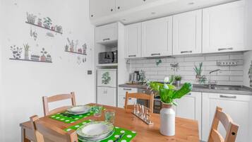 Una cucina moderna con mobili bianchi, un tavolo da pranzo in legno con sottopiatti verdi e diversi elettrodomestici.
