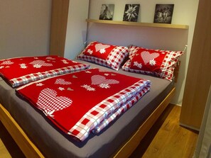 Un lit avec une couvre-lit à carreaux rouges et blancs et des coussins assortis, une tête de lit en bois et une étagère avec des photos encadrées au-dessus.