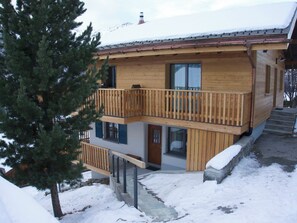 Eine zweistöckige Holzdiele mit einem Balkon, einem mit Schnee bedeckten Dach und Blick auf einen Berg.