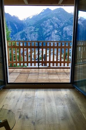 Ein Zimmer mit Holzboden, einer Glastür zu einem Balkon mit Holzgeländer und Bergblick.